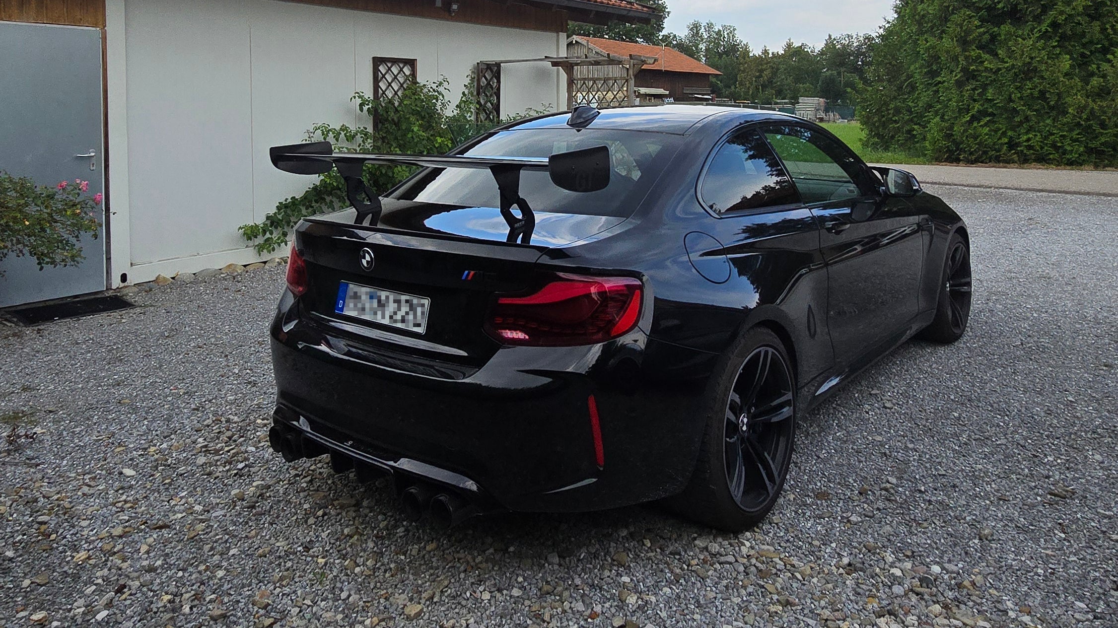 Schwarzer BMW M2 F87 mit installiertem Aero Heckflügel GT Flex Carbon auf einem Kiesboden, zeigt das sportliche Design und die verbesserte Aerodynamik nach der professionellen Montage und TÜV-Eintragung bei Stefanel Performance.
