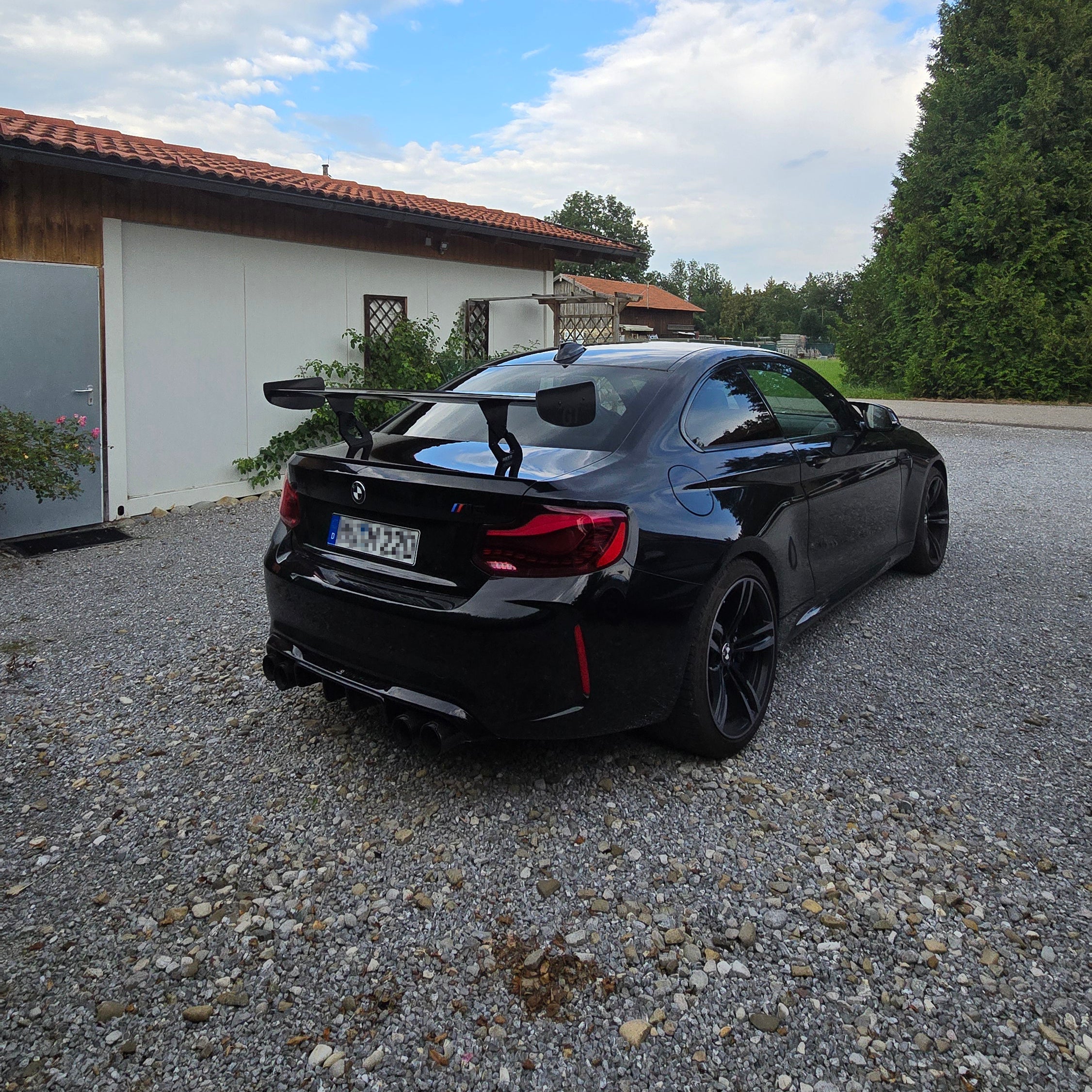 Schwarzer BMW M2 F87 mit installiertem Aero Heckflügel GT Flex Carbon auf einem Kiesboden, zeigt das sportliche Design und die verbesserte Aerodynamik nach der professionellen Montage und TÜV-Eintragung bei Stefanel Performance.